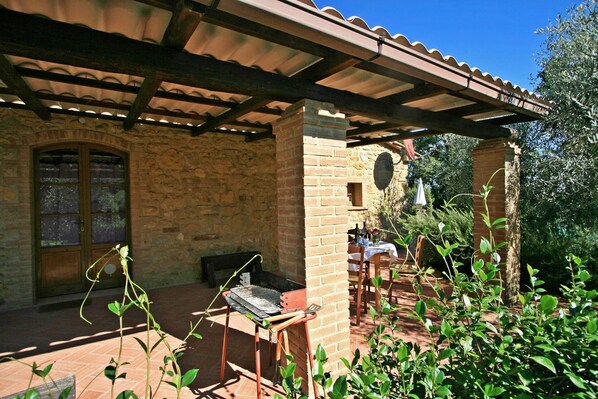 A covered outdoor area with a brick wall, a grill, and a table with chairs. - Cozy, pet-friendly vacation home with a private pool in Tuscany (Pomarance)