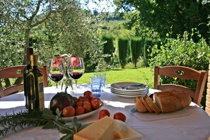 A table set outdoors with a bottle of wine, glasses, a plate of tomatoes, a loaf of bread, and a small bowl of cheese. - Cozy, pet-friendly vacation home with a private pool in Tuscany (Pomarance)