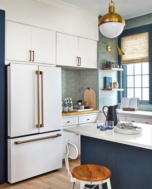 Une cuisine moderne avec des meubles blancs, un grand réfrigérateur, un îlot central en bois doté de sièges et une fenêtre offrant une belle vue.
