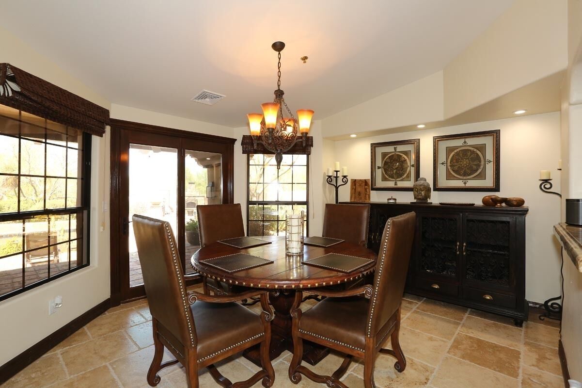 A dining room with a round wooden table, four chairs, a chandelier, and a black cabinet with decorative items.