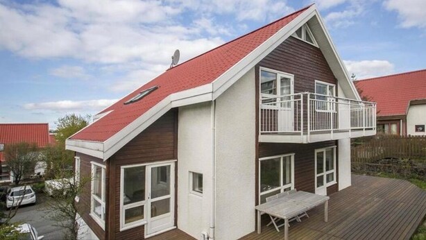 A two-story house with a red roof, a balcony on the upper floor, and a wooden deck. - Great villa in the center of Reykjavik on the most beautiful valley of the town (Unknown)
