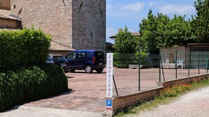 Ein Parkbereich mit einem Schild, das einen Stellplatz anzeigt, ein blauer Wagen und ein Gebäude mit einer Ziegelwand im Hintergrund.