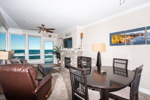 A dining area with a stone fireplace, a ceiling fan, and a view of the ocean through large windows.
