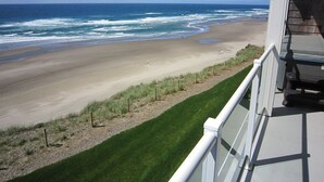 Strandudsigt fra en balkon med gelænder, havnebølger og en klar himmel.