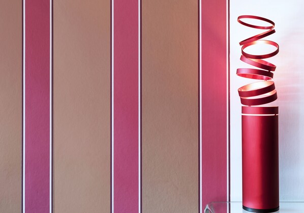 A red cylindrical object with a spiral design against a wall with vertical stripes. - Orchid Apartment - charming apartment in the center of Rome (Roma)
