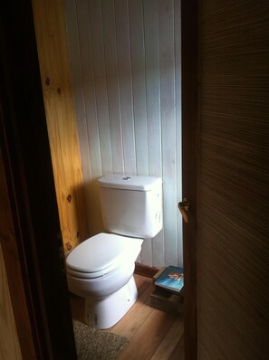 Un baño pequeño y funcional con inodoro blanco, paredes de madera y una puerta.