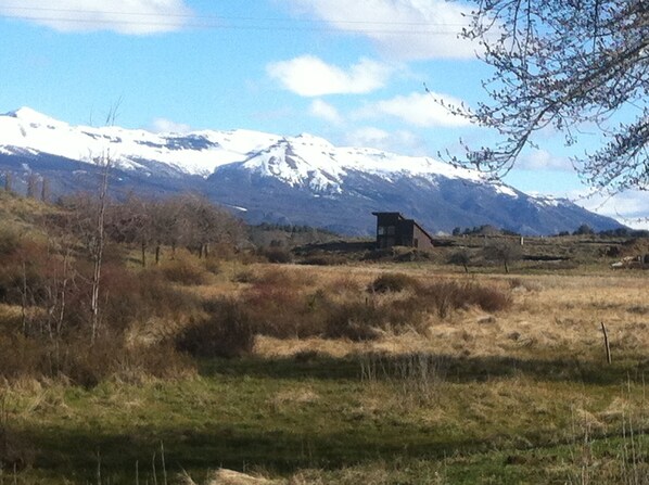 Paisaje rural con un edificio pequeño, montañas nevadas y cielo despejado.