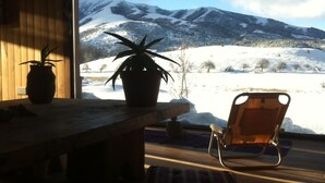 A wooden table with two potted plants, a wooden chair, and a view of a snowy landscape with mountains. - Your Home In The Andes (San Martin de los Andes)