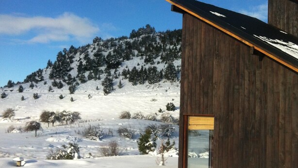 A wooden cabin with a glass door, surrounded by a snowy landscape and a forested hill. - Your Home In The Andes (San Martin de los Andes)