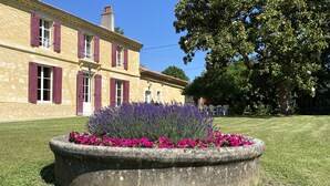 Un bâtiment en pierre avec des volets rouges et un jardin agrémenté de lavande et de fleurs roses.