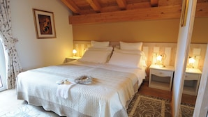 Une chambre avec un plafond en bois, un lit recouvert de draps blancs, deux tables de chevet avec des lampes et un tableau encadré au mur.