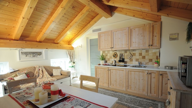 Une cuisine chaleureuse avec des meubles en bois, un coin repas avec une table dressée pour deux personnes, et un salon avec un canapé et une cheminée.