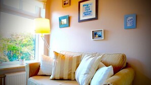 Una stanza accogliente con un divano color beige, una finestra con vista sul verde e diverse foto incorniciate appese al muro.