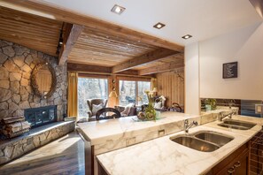 Una cucina moderna con camino in pietra, travi in legno al soffitto e un piano di lavoro in marmo.