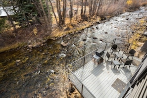 Una terrazza con posti a sedere all'aperto affacciata su un fiume, circondata da alberi e da un pontile in legno.