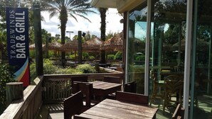 Un espace extérieur aménagé avec des tables et des chaises en bois, entouré d’une végétation luxuriante et de palmiers.