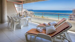 A balcony with white chairs and a table, a striped lounge chair, and a view of the sea. - FRONTLINE APARTMENT WITH BIG TERRACE AND BEATIFULL SEA VIEWS (Calpe)