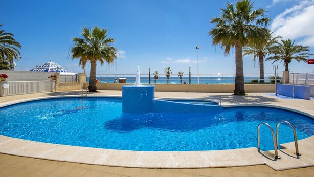 A swimming pool with a fountain, surrounded by palm trees and a view of the ocean. - FRONTLINE APARTMENT WITH BIG TERRACE AND BEATIFULL SEA VIEWS (Calpe)