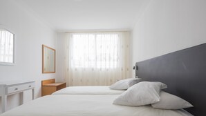 Una camera da letto con due letti, un comodino, uno specchio e una finestra con tende.