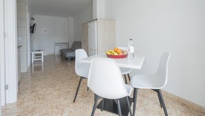 Zona pranzo moderna e minimalista, con un tavolo bianco, quattro sedie bianche e una ciotola di frutta.