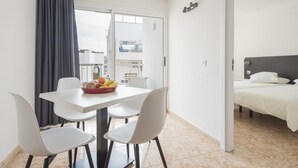 Una moderna camera d'albergo con un balcone, un'area pranzo con tavolo e sedie, e un letto con biancheria da letto bianca.