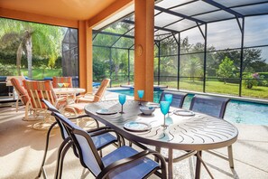 Patio esterno con tavolino da biliardo, sedie e zona coperta vista piscina e giardino.
