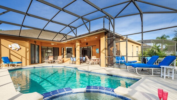 Ein Swimmingpool mit blau gefliesten Rändern, umgeben von Liegestühlen und einer überdachten Terrasse.