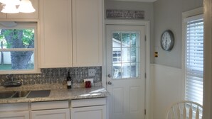 A kitchen with white cabinets, a window, a welcome sign, a clock, and a dining area with a wooden table. - Great Location!  Come Relax....Retreat!   (Kerrville)