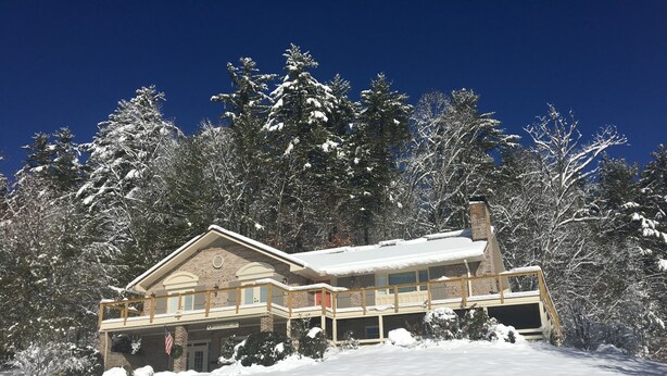 A wooden cabin with a balcony, surrounded by snow-covered trees.