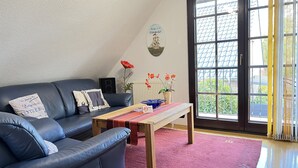 Een woonkamer met een donkerblauwe leren bank, een houten salontafel en een roze vloerkleed.