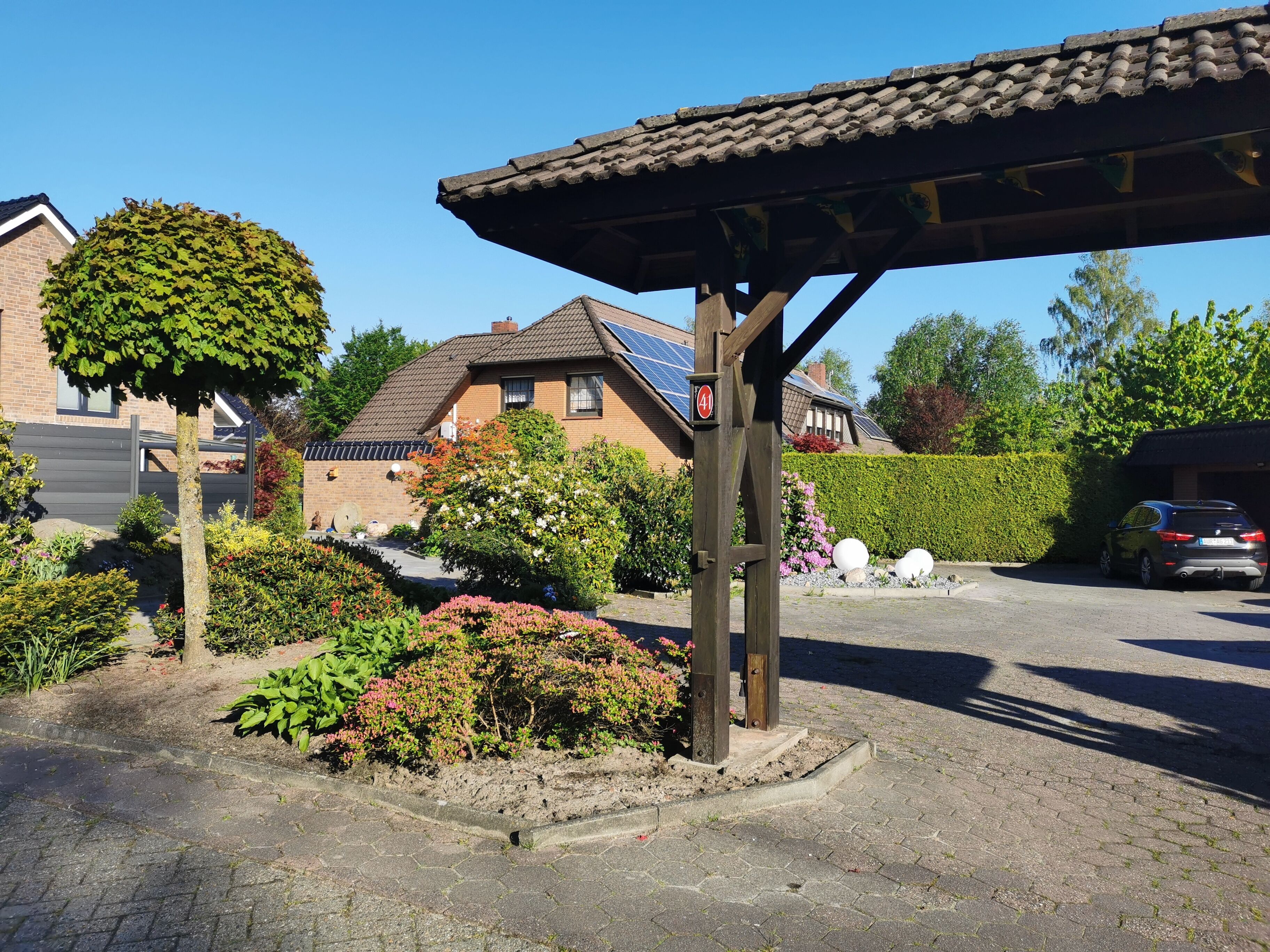 Un barrio residencial con un camino de entrada pavimentado, una pérgola de madera y una casa con paneles solares.