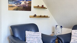 Een kamer met twee leren fauteuils, een schilderij van een vuurtoren en houten planken met decoratieve objecten.