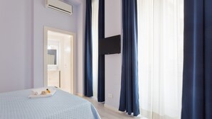 Une chambre à coucher avec un lit, un téléviseur à écran plat fixé au mur et une fenêtre avec des rideaux.