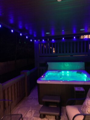 Uma banheira de hidromassagem com deck e guarda-corpo de madeira, rodeada por luzes de Natal.