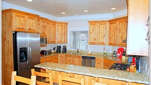 Eine Küche mit Holzausbau, einem Edelstahlkühlschrank, einer Granitarbeitsplatte und einer Bar mit Holzstühlen.