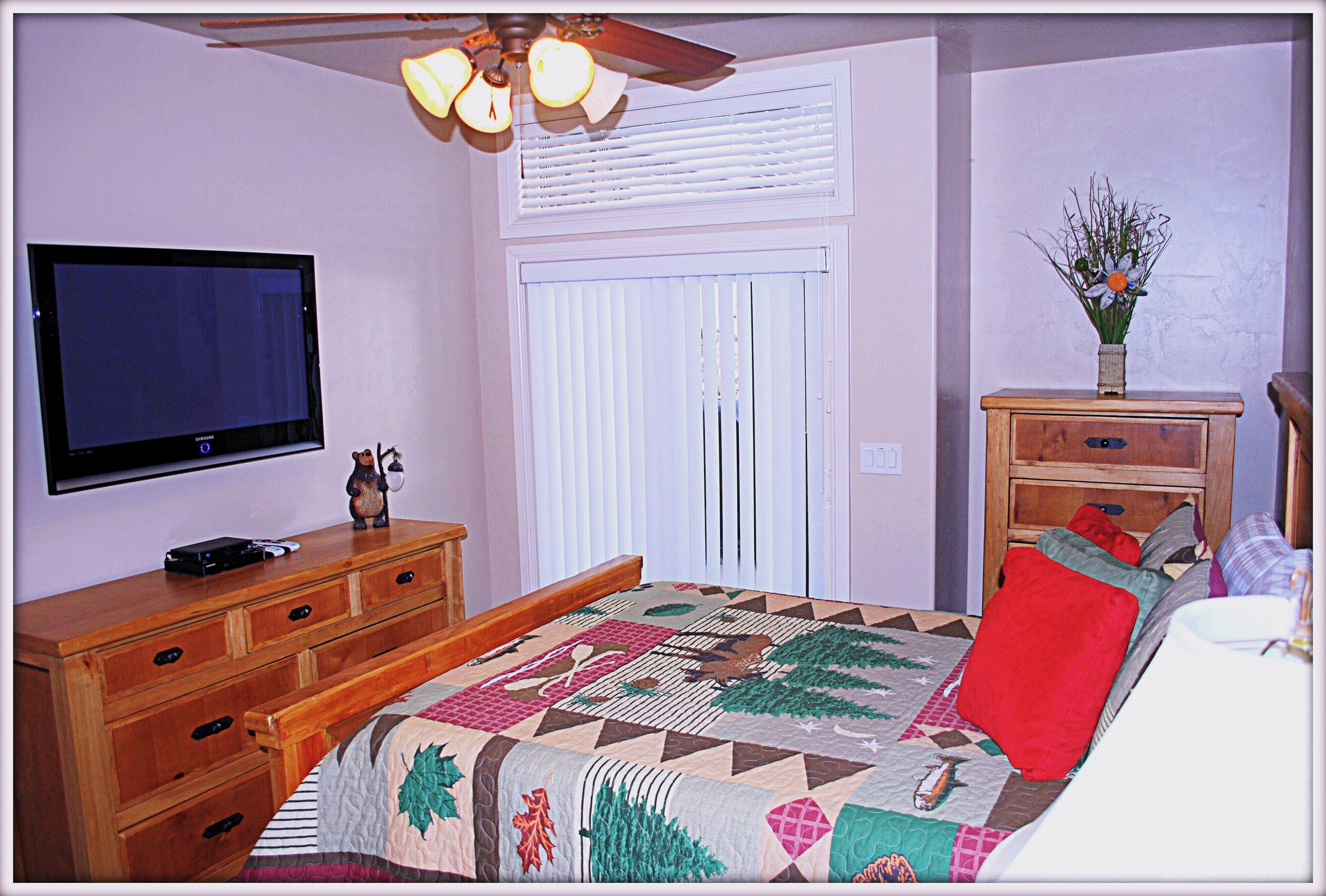 Ein Schlafzimmer mit Bett, Kommode, Fernseher und Deckenventilator.