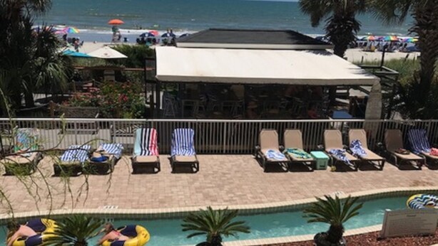 Ein Poolbereich mit Liegestühlen und Sonnenschirmen, ein Pool mit Wasserrutschen und Blick aufs Meer.