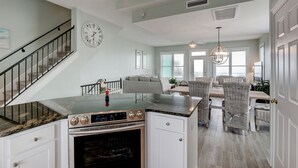 A modern kitchen with a built-in oven, a dining area with wicker chairs, and a staircase with black railings. - 🌞Oceanfront rooftop getaway 🏖️Steps to sand 🐶Dog Friendly⚡️EV charger (North Topsail Beach)
