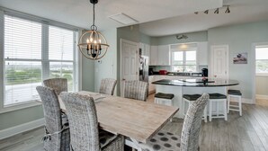 A kitchen with a central island, white cabinetry, and a dining area with wicker chairs. - 🌞Oceanfront rooftop getaway 🏖️Steps to sand 🐶Dog Friendly⚡️EV charger (North Topsail Beach)
