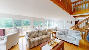 Uma sala de estar espaçosa com grandes janelas, uma escada e um deck de madeira.