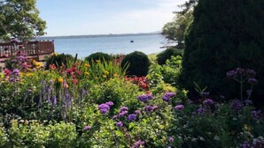 Um jardim com diversas flores e um deque de madeira com vista para a água.