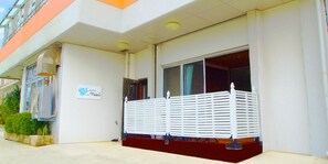 A building with a white exterior, a sign that reads "Watch," and a white fence in front. - Rental Villa Lana Waioli (Tomigusuku)