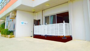 A building with a white and orange facade, a covered entrance, and a small garden area. - Rental Villa Lana Waioli (Tomigusuku)