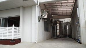 A narrow corridor with industrial tanks, a white fence, and a manhole cover. - Rental Villa Lana Waioli (Tomigusuku)