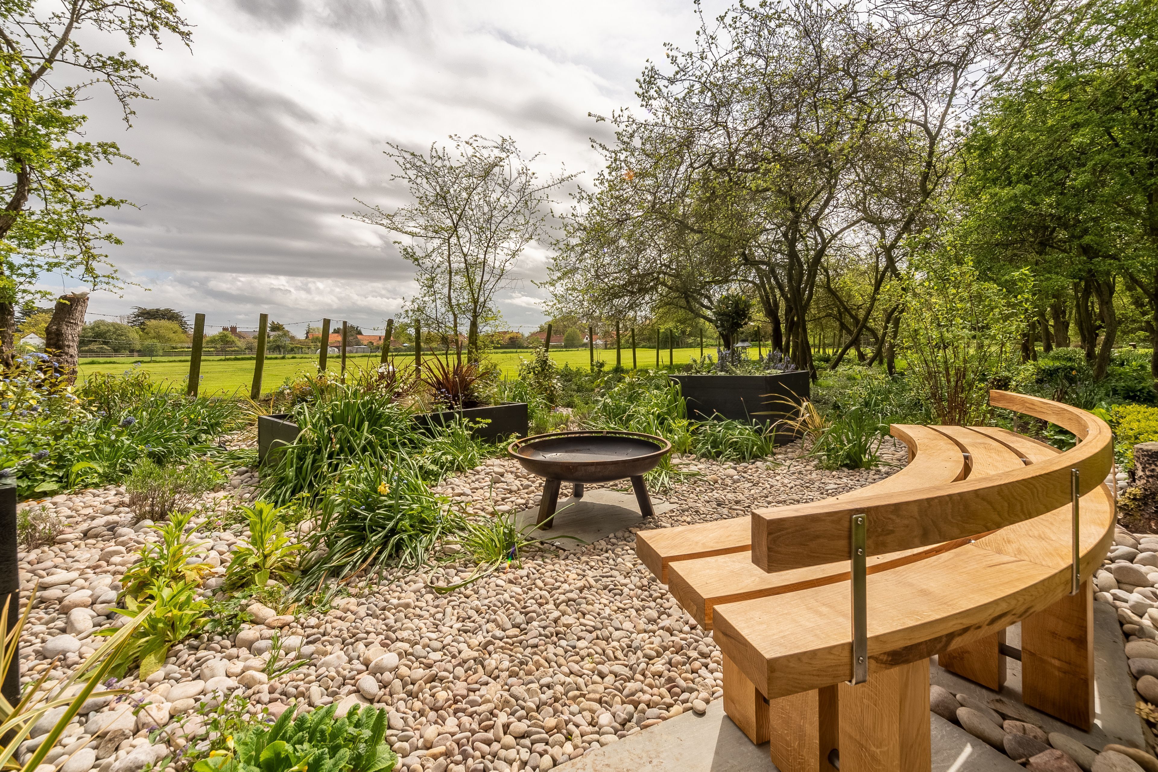 A garden with a wooden bench, a fire pit, and a variety of plants.