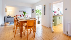 A modern living room with a wooden dining table, chairs, and a grey sofa. There is a potted plant and artwork on the walls. - Sybil Cottage, Holme-next-the-Sea, Norfolk (Hunstanton)