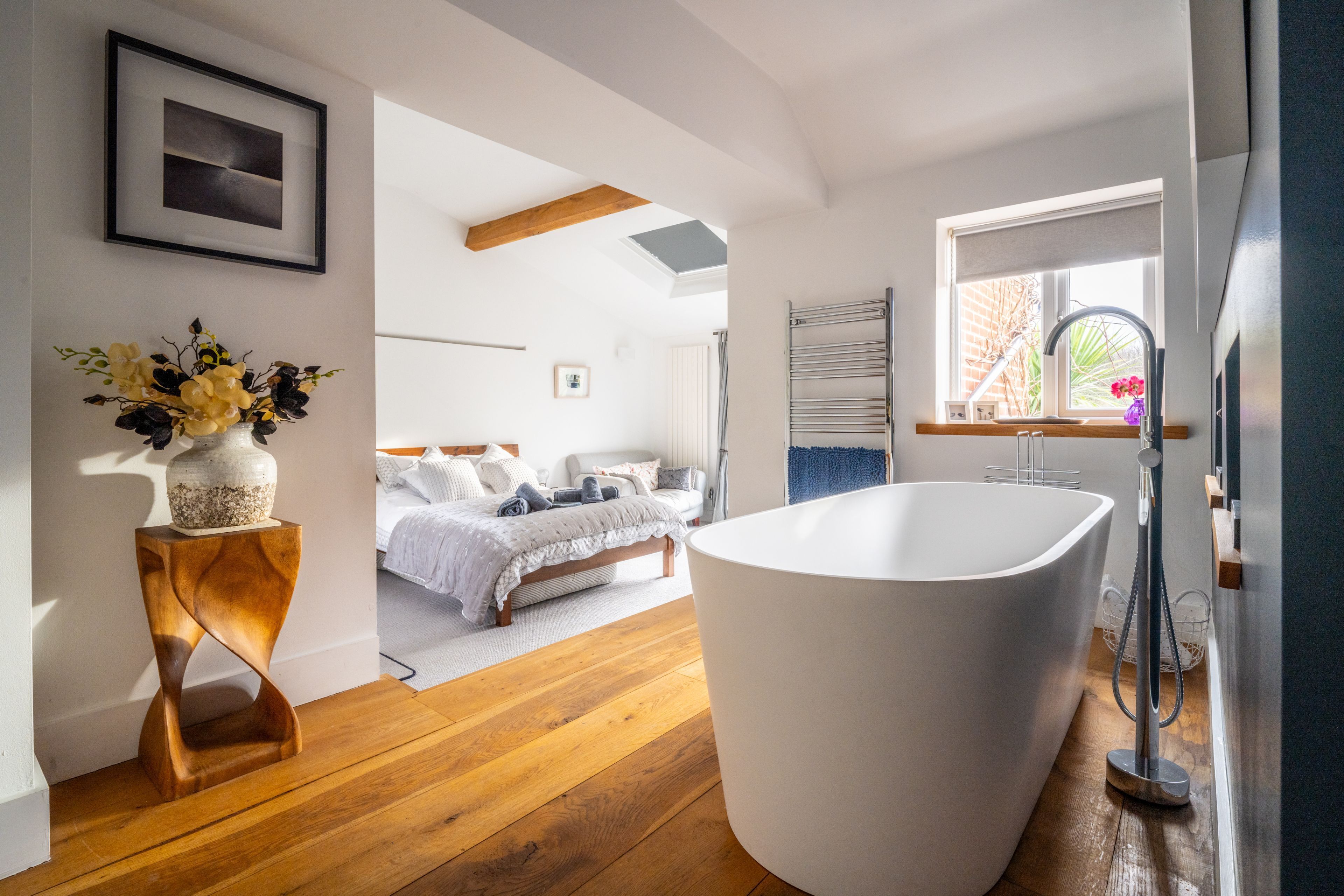 Un baño moderno con una bañera independiente, suelo de madera y un ventanal con vistas al exterior.