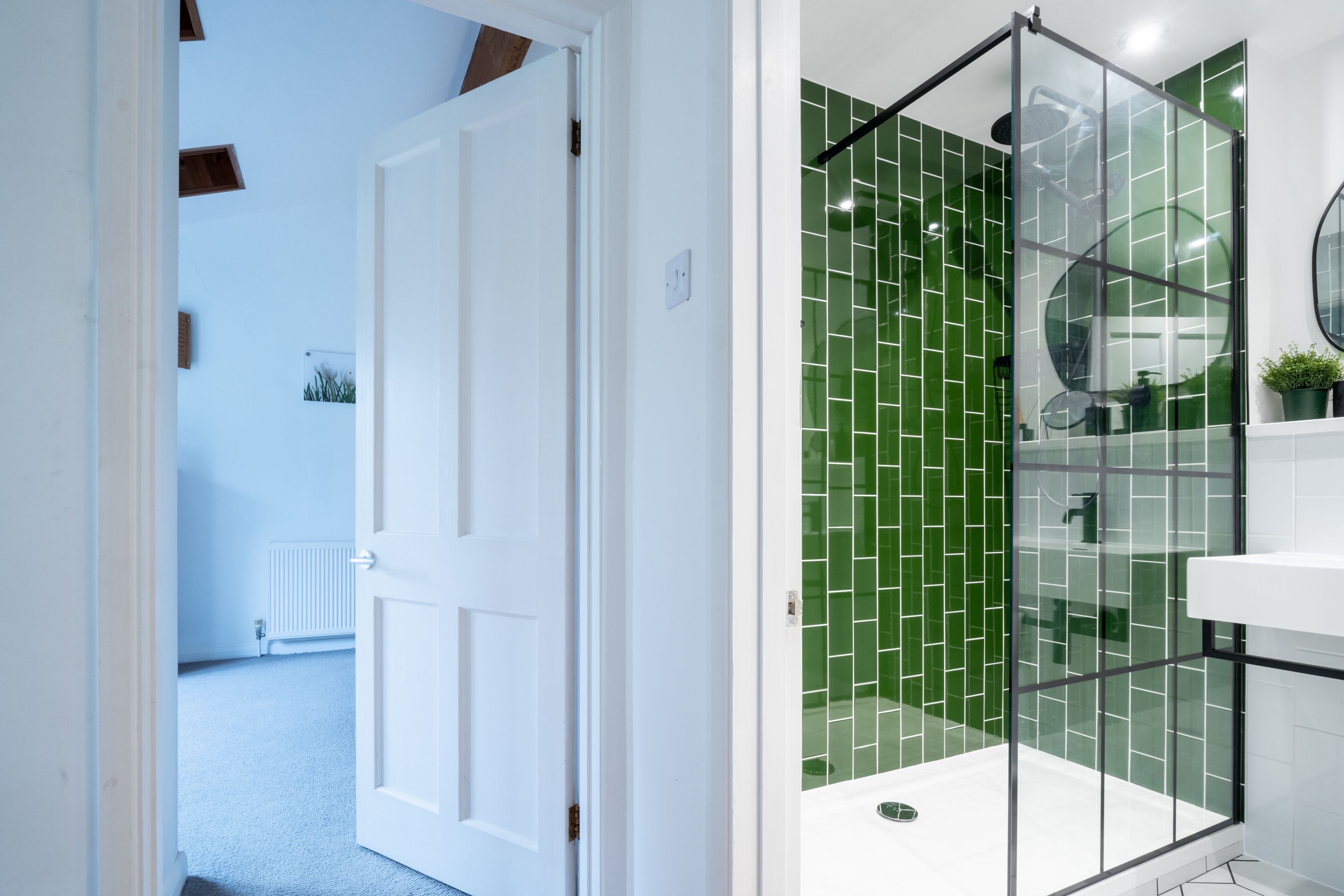 A modern bathroom with a glass shower enclosure, white fixtures, and a green-tiled shower wall.