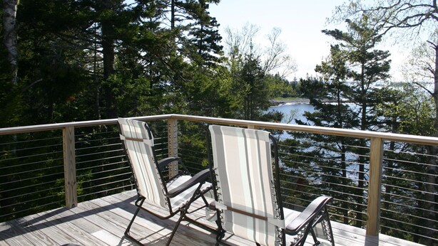 A wooden deck with two chairs facing a lake, surrounded by trees. - Tranquil oceanfront cottage on Wohoa Bay (Addison)