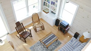 A room with a wooden floor, a rocking chair, a sofa, a small table, and a bookshelf. - Tranquil oceanfront cottage on Wohoa Bay (Addison)